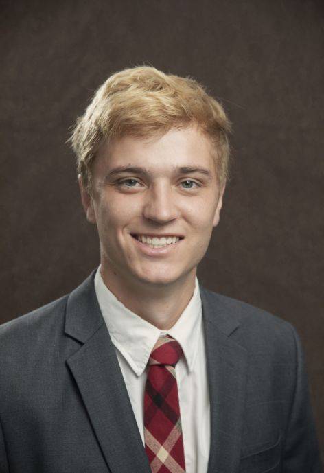 Logan Jensen wearing a grey jacket, white button-up, and red tie.
