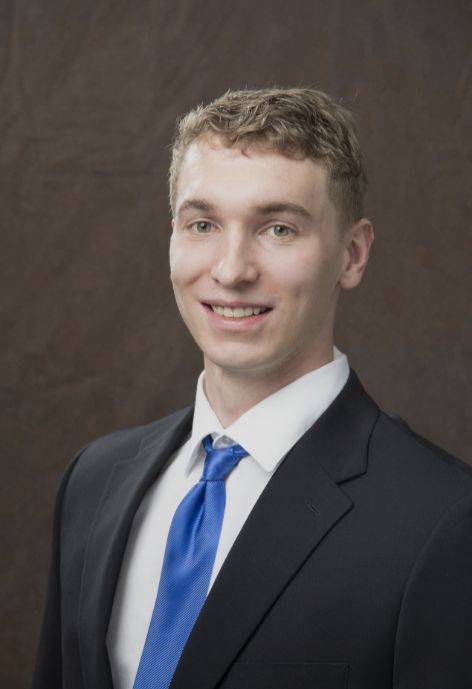 Winston Littlejohn wearing a black suit jacket, white button-up, and blue tie.