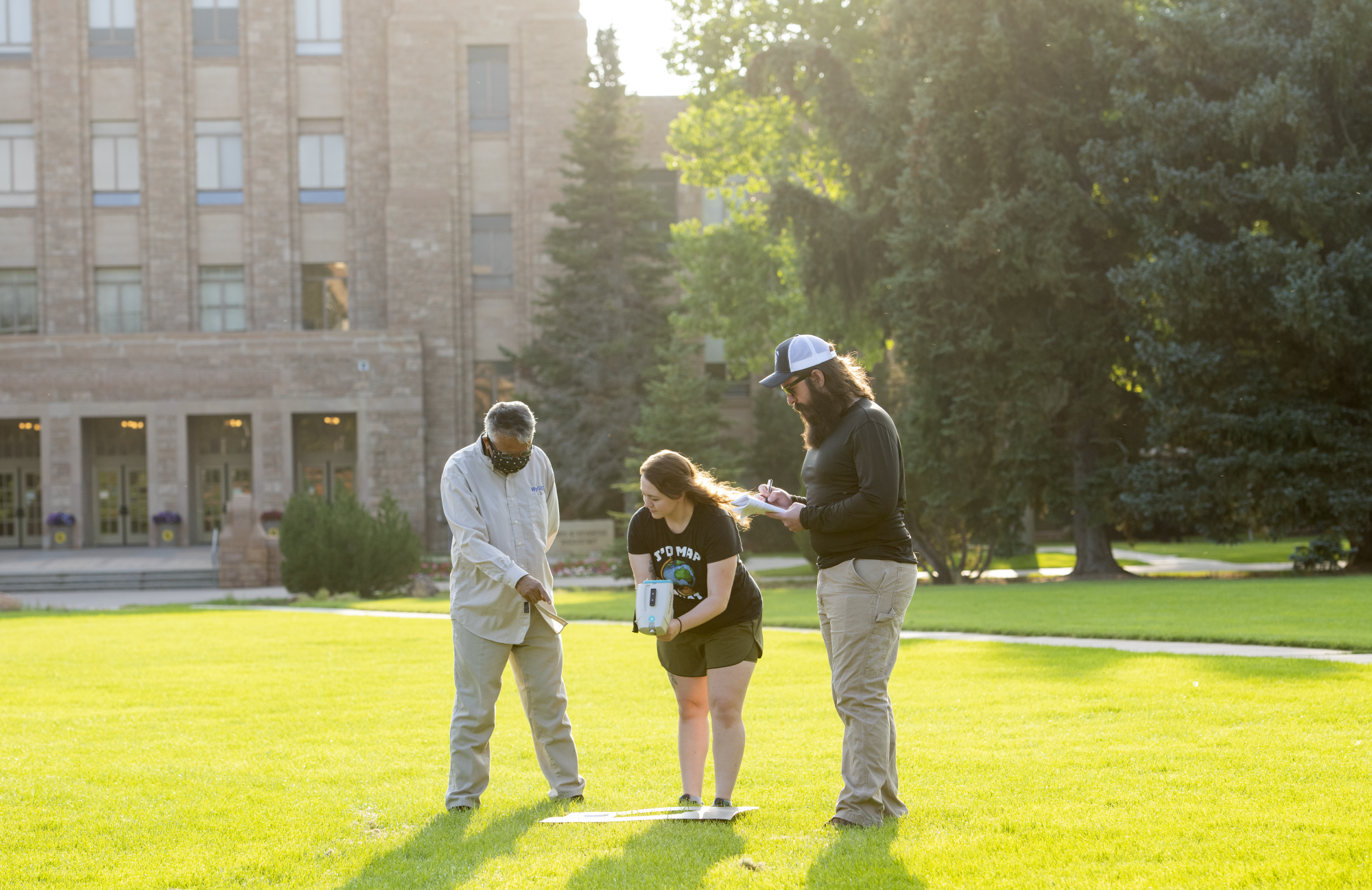 Three people standing outside looking at a remote sensing tool.