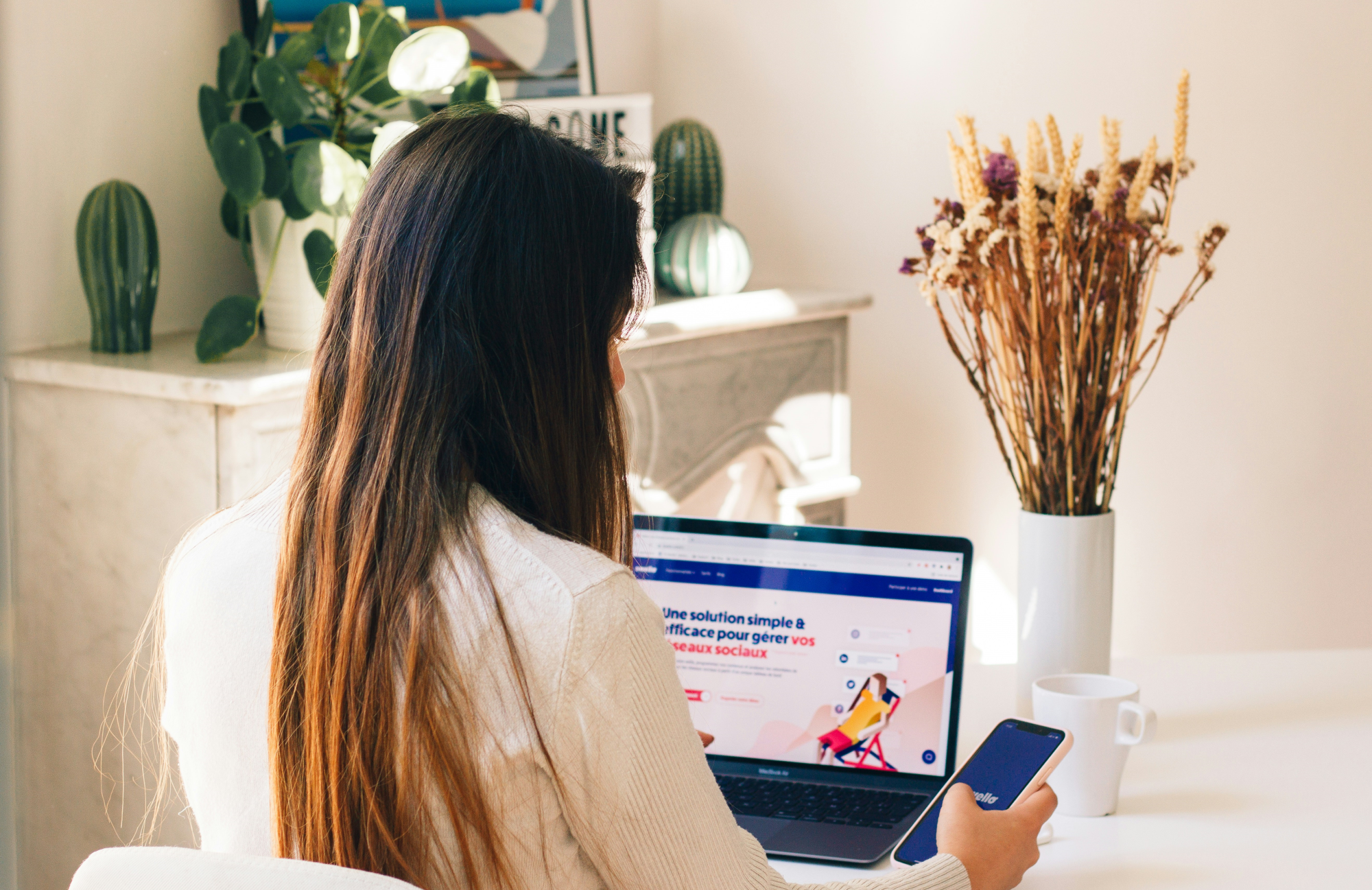 A women looking at a phone with a laptop open in front of her.