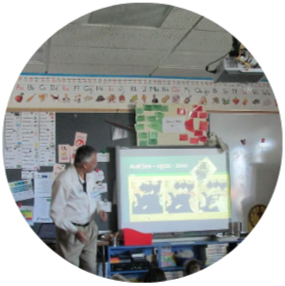 A teacher speaking at the front of a classroom.