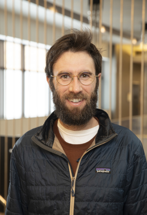 Ben Koger smiles, wearing a black jacket and glasses.