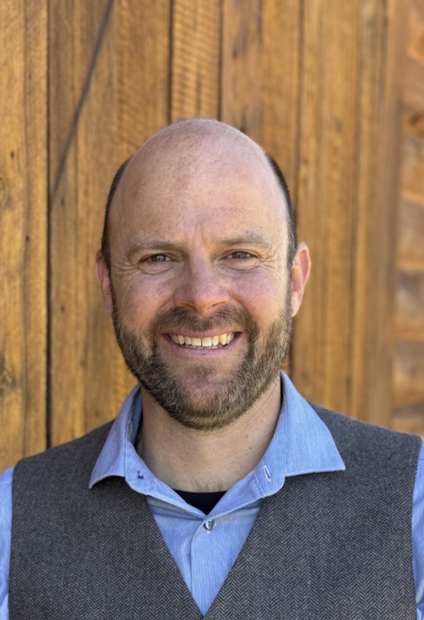 Jerod Merkle smiles, standing in front of a wooden wall.