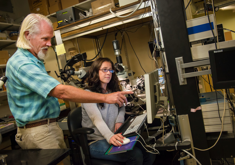 A gentleman instructs a woman using a microscope.